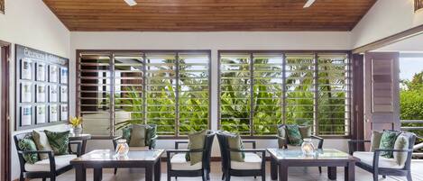 Un vaste espace intérieur doté d’un plafond en bois et de grandes fenêtres, offrant une vue sur la verdure luxuriante environnante.