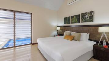 A hotel room with a large bed, two bedside tables, a wall-mounted air conditioner, and a view of a pool through a sliding glass door.