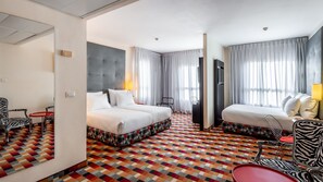 A hotel room with a large bed, a smaller bed, a desk, a chair, a TV, and a patterned floor. - Jacob Harmony Jerusalem (Jerusalem)