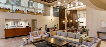 Un vestíbulo amplio con mostrador de recepción, zona de estar y ventanas grandes.