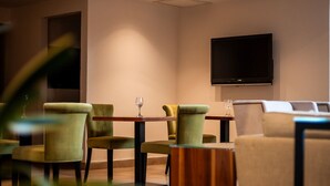 A hotel lobby with green upholstered chairs, a flat-screen TV mounted on the wall, and a sofa with a white cover.