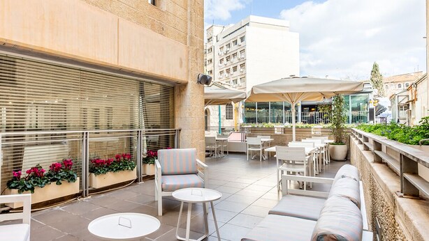 An outdoor patio with seating, planters with flowers, and a view of the cityscape.