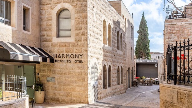 A Harmony Hotel with a stone facade, a striped awning, and a narrow street view.
