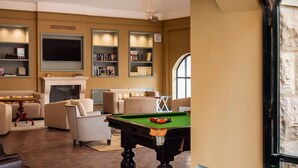 A living room with a pool table, sofas, a fireplace, and bookshelves.