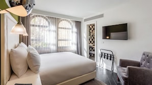 A modern hotel room with a large bed, a TV mounted on the wall, a seating area with a chair, and a small table.