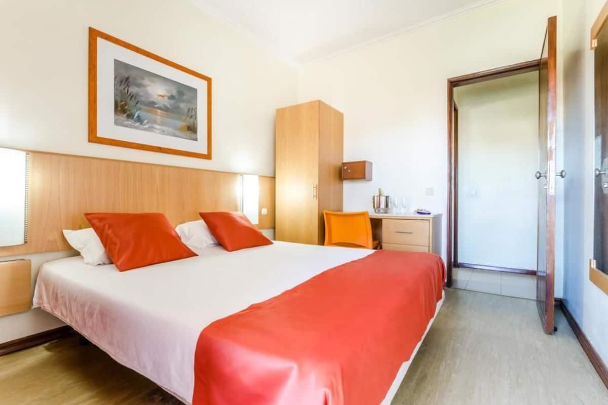 Una habitación de hotel con una cama, un escritorio, una silla, un armario y una puerta.