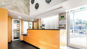 Un área de recepción con un mostrador de madera, una puerta de cristal que da a una sala de espera y vistas al estacionamiento exterior.