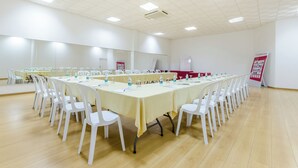 Un salón de conferencias con una larga mesa, sillas blancas y un cartel rojo en la pared.