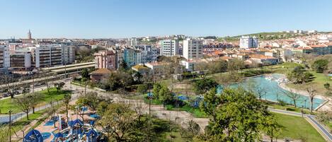 A park with playgrounds and a swimming pool, surrounded by buildings and a clear sky.