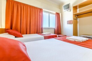 Een hotelkamer met twee bedden, oranje gordijnen, een aan de muur bevestigde televisie en een houten plank met een kapstok.