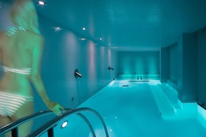 A modern indoor swimming pool with a glass wall, a clear water path, and a person using the pool's edge. - Sweet Atlantic Hotel & Spa (Figueira da Foz)