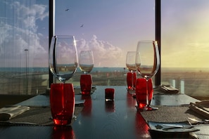 A table with four wine glasses and a red bottle, set against a view of the sea and sky. - Sweet Atlantic Hotel & Spa (Figueira da Foz)