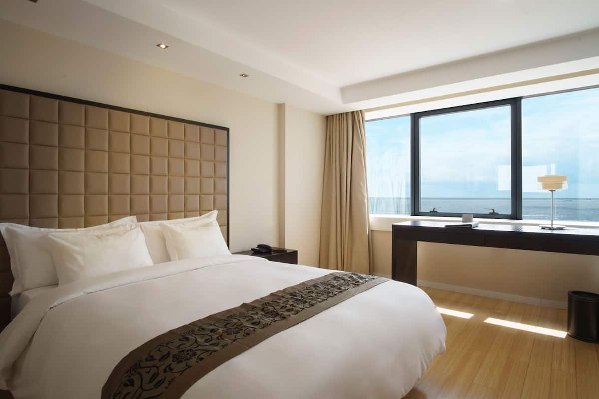 A hotel room with a large bed, a desk with a view of the sea, and a modern design.