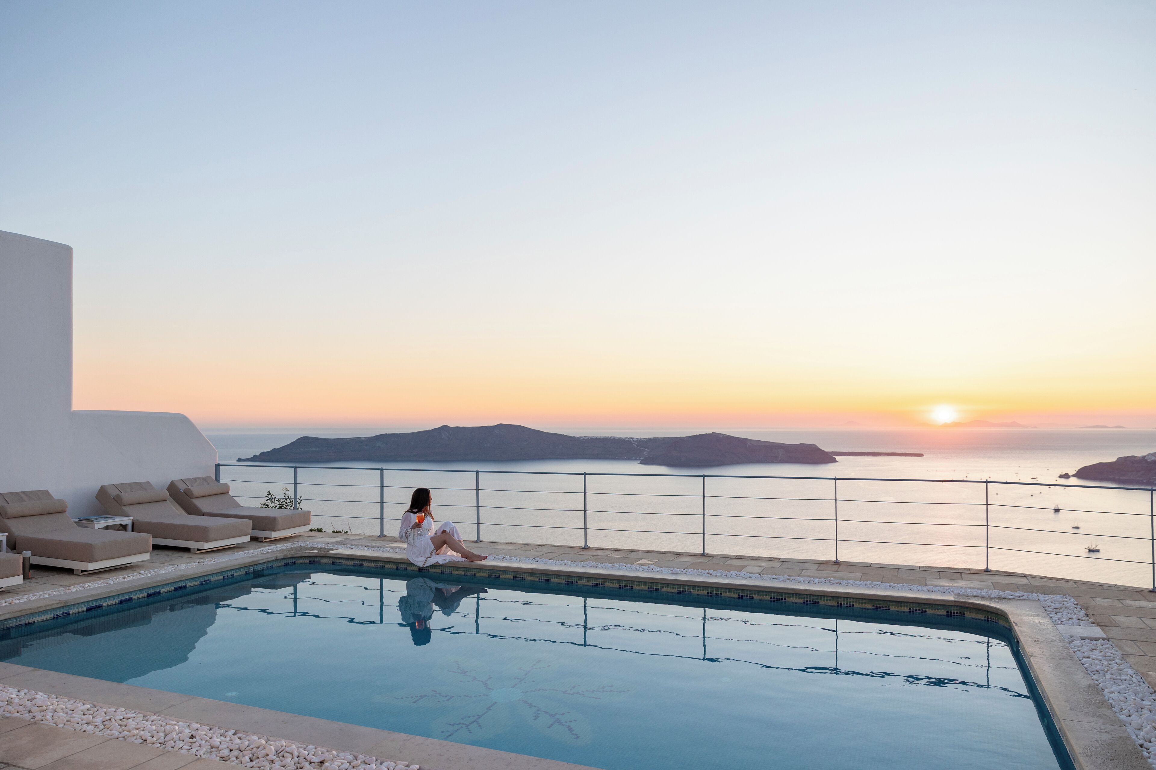 Zona de piscina con sillones de descanso y vista al mar al atardecer.