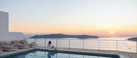Zona de piscina con sillones de descanso y vista al mar al atardecer.