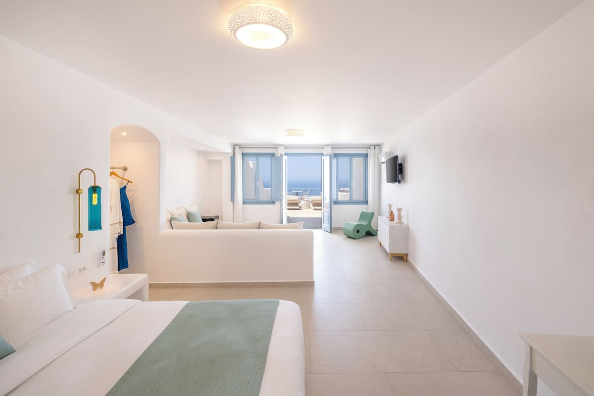 A spacious bedroom with a large bed, a seating area with a view, and a bathroom with a shower and a towel rack.