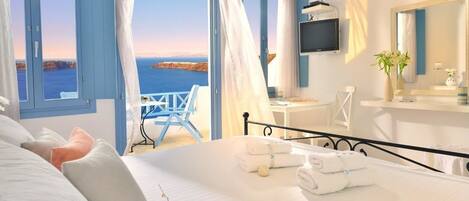 A bedroom with a bed, a TV, a desk, and a view of the sea.