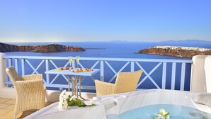 Un balcón con hidromasaje, sillas de mimbre, una mesa con comida y bebidas, y vistas al mar y a los acantilados.