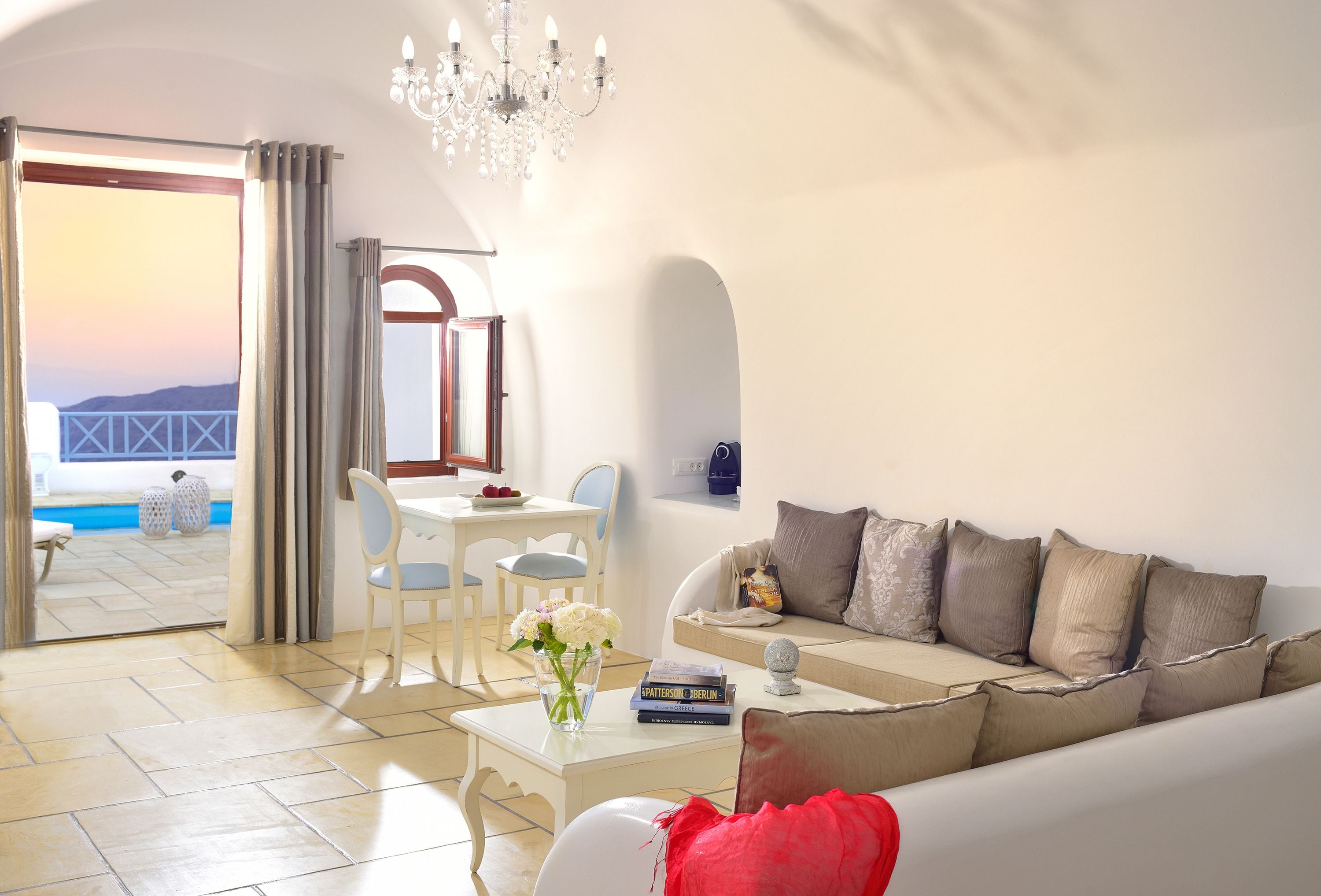 A living room with a sofa, a coffee table with a vase, a dining area with chairs, and a view of the sea through a large window.