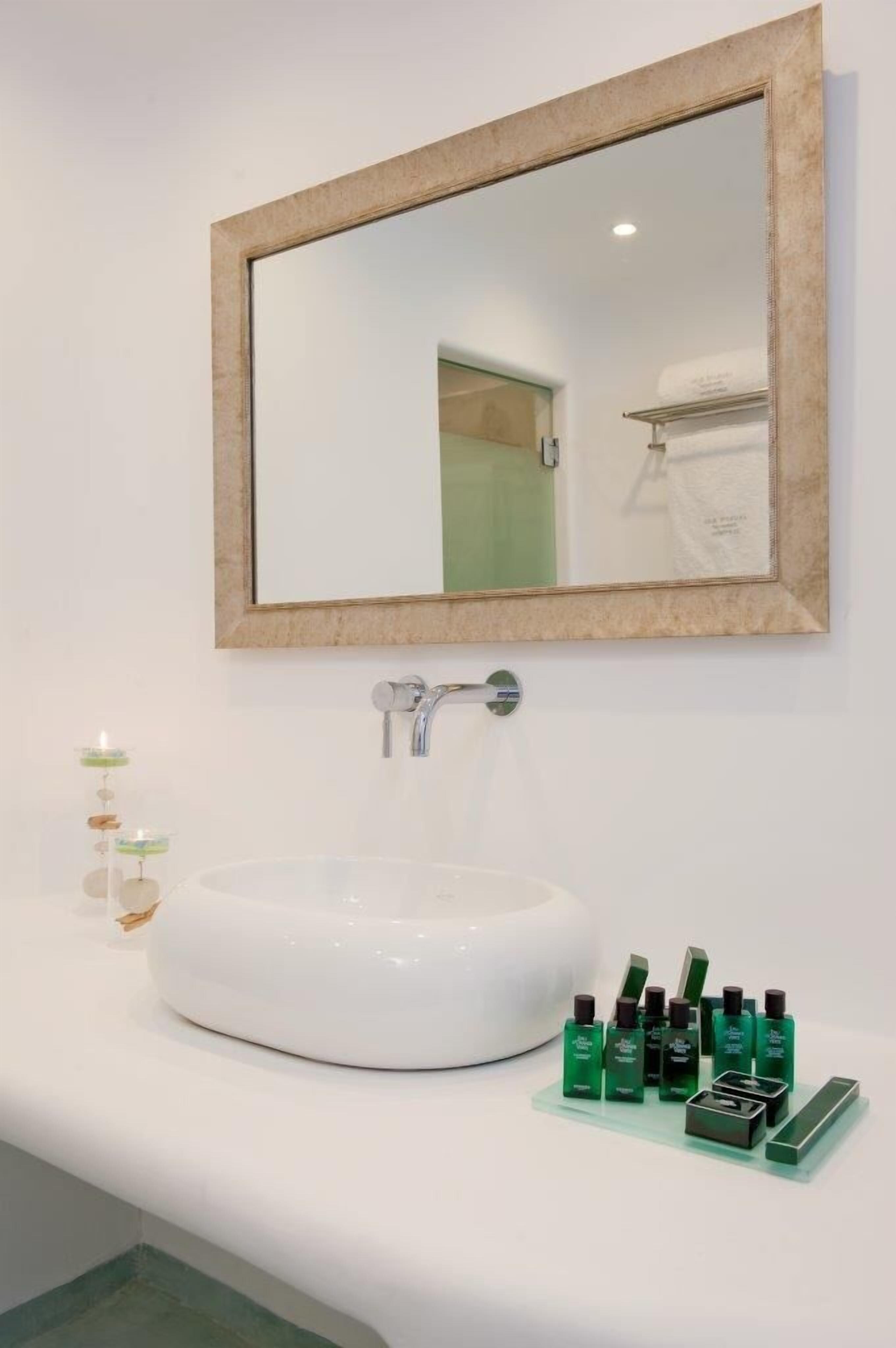 A bathroom with a white sink, a mirror with a wooden frame, and a row of green bottles on the counter.