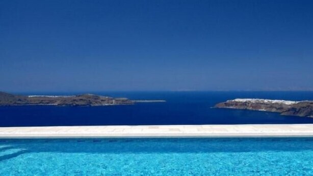 A clear view of a swimming pool with a horizon of rocky islands and the sea. - Absolute Bliss (Santorini)