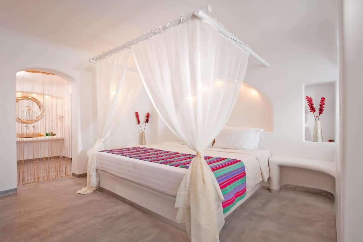 A modern bedroom with a canopy bed, a bedside table, a mirror, and a small seating area with a bench.