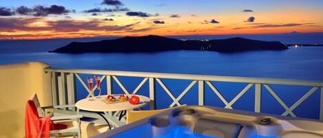 A balcony with a hot tub, a table with drinks, and a view of the sea at sunset.