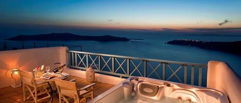 Un balcón con jacuzzi, mesa y sillas, con vistas a la costa al atardecer.
