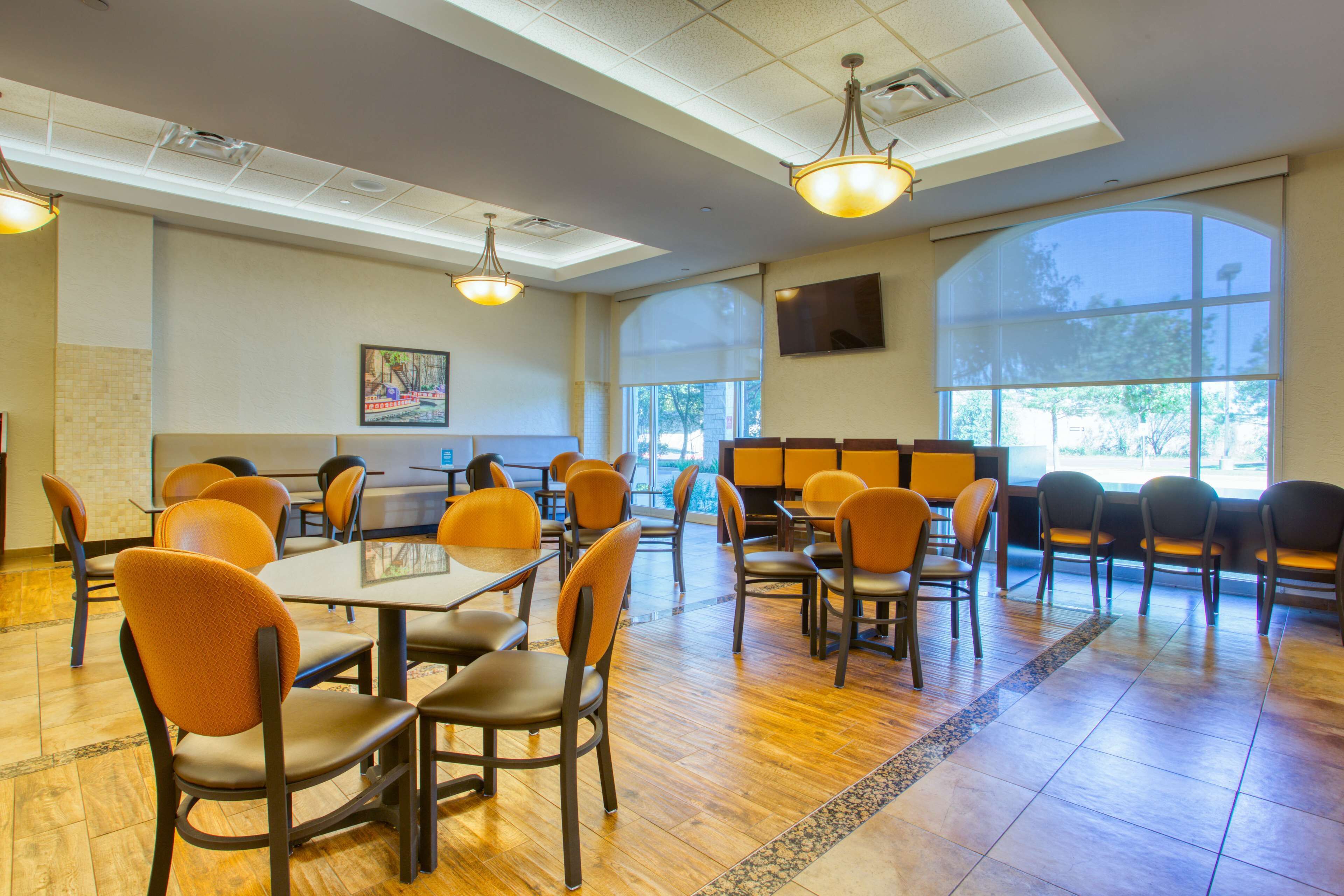 A spacious dining area with high tables and chairs, large windows, and a modern ceiling design.