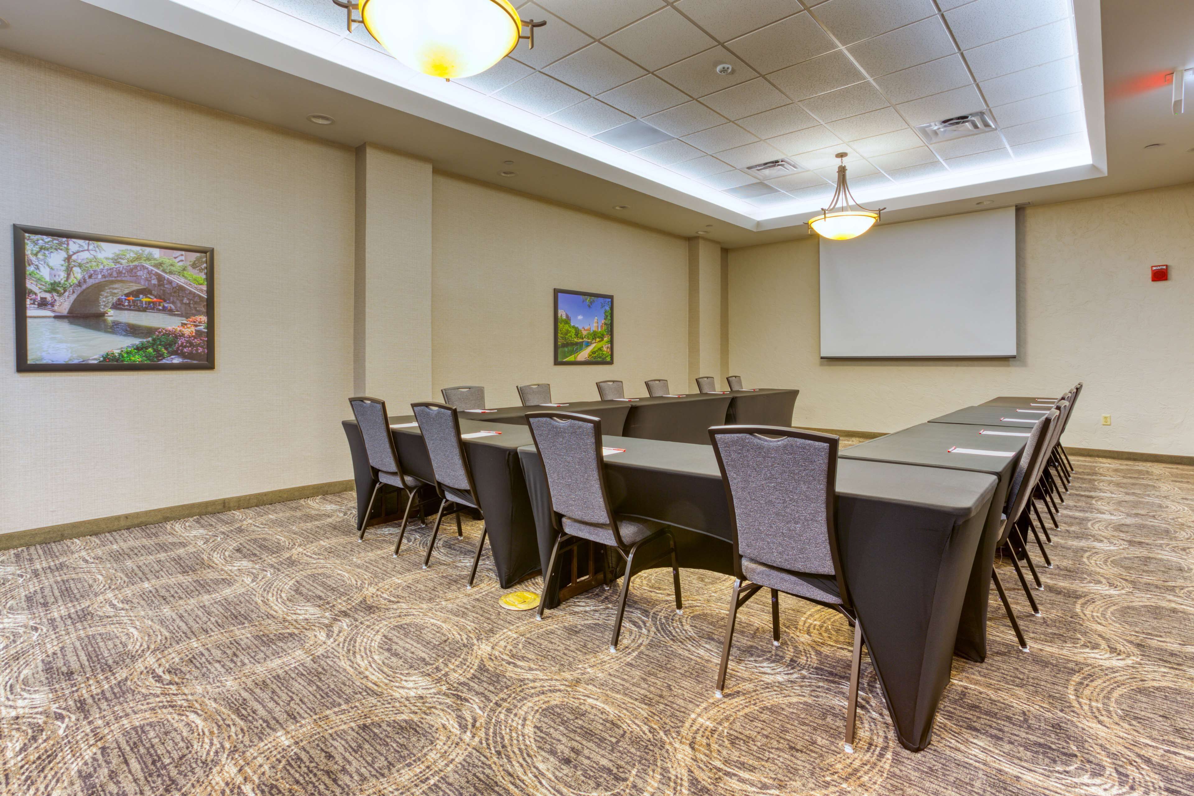 A conference room with a long table, chairs, a projector screen, and two wall-mounted lights.