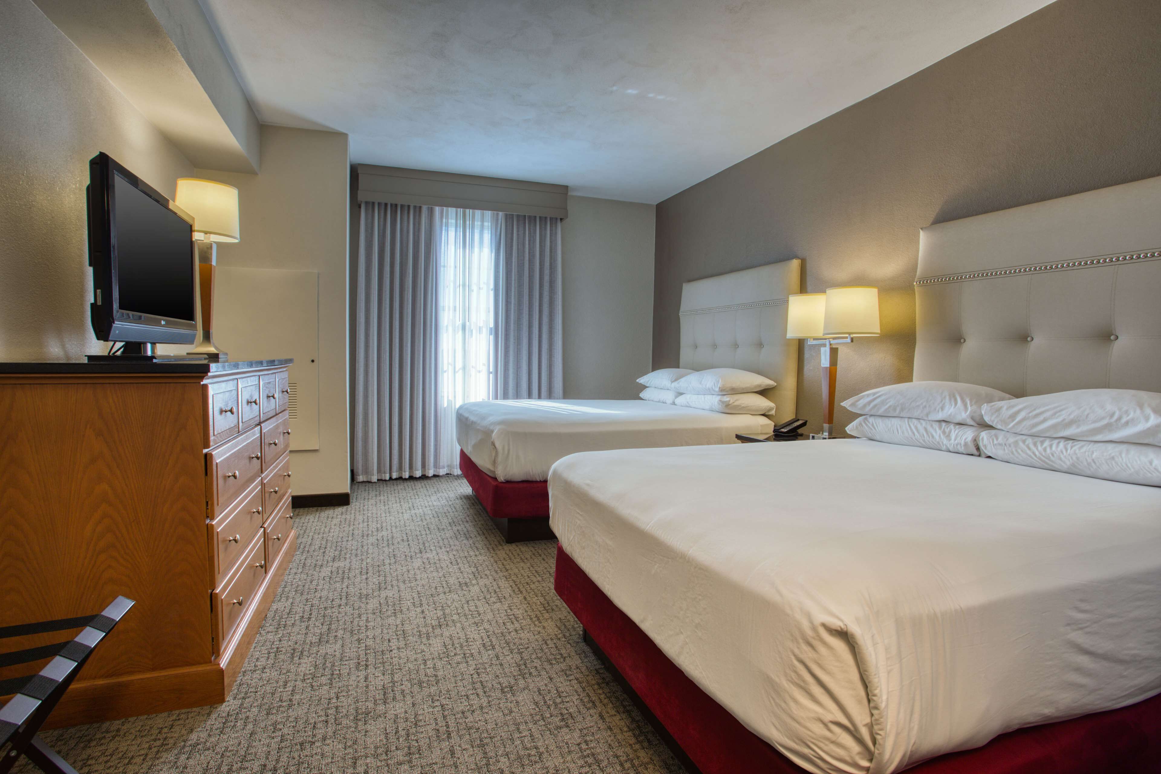 Habitación de hotel con dos camas, un televisor, un aparador y una ventana con cortinas.