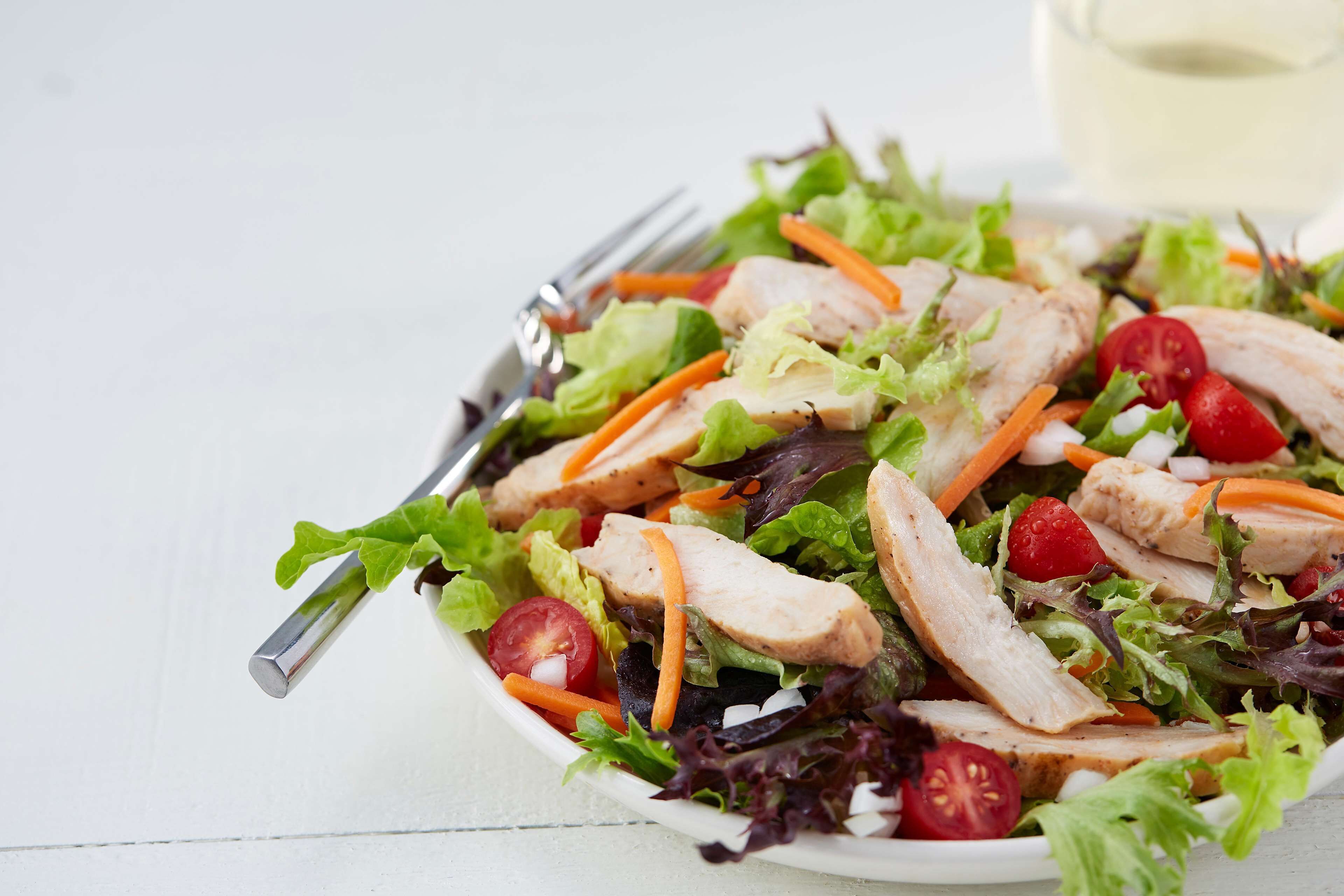 Ensalada con lechuga, tomates, zanahorias y lonchas de pollo.