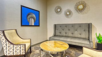 Une pièce avec un canapé gris, un fauteuil à motifs et une table basse ronde en verre.