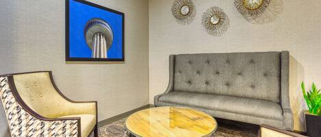 A room with a grey sofa, patterned armchair, and a round glass coffee table.