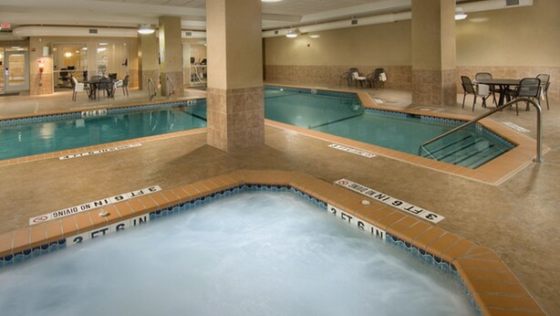 Een binnenzwembad met een jacuzzi, betegelde vloer en een zitgedeelte met tafels en stoelen.