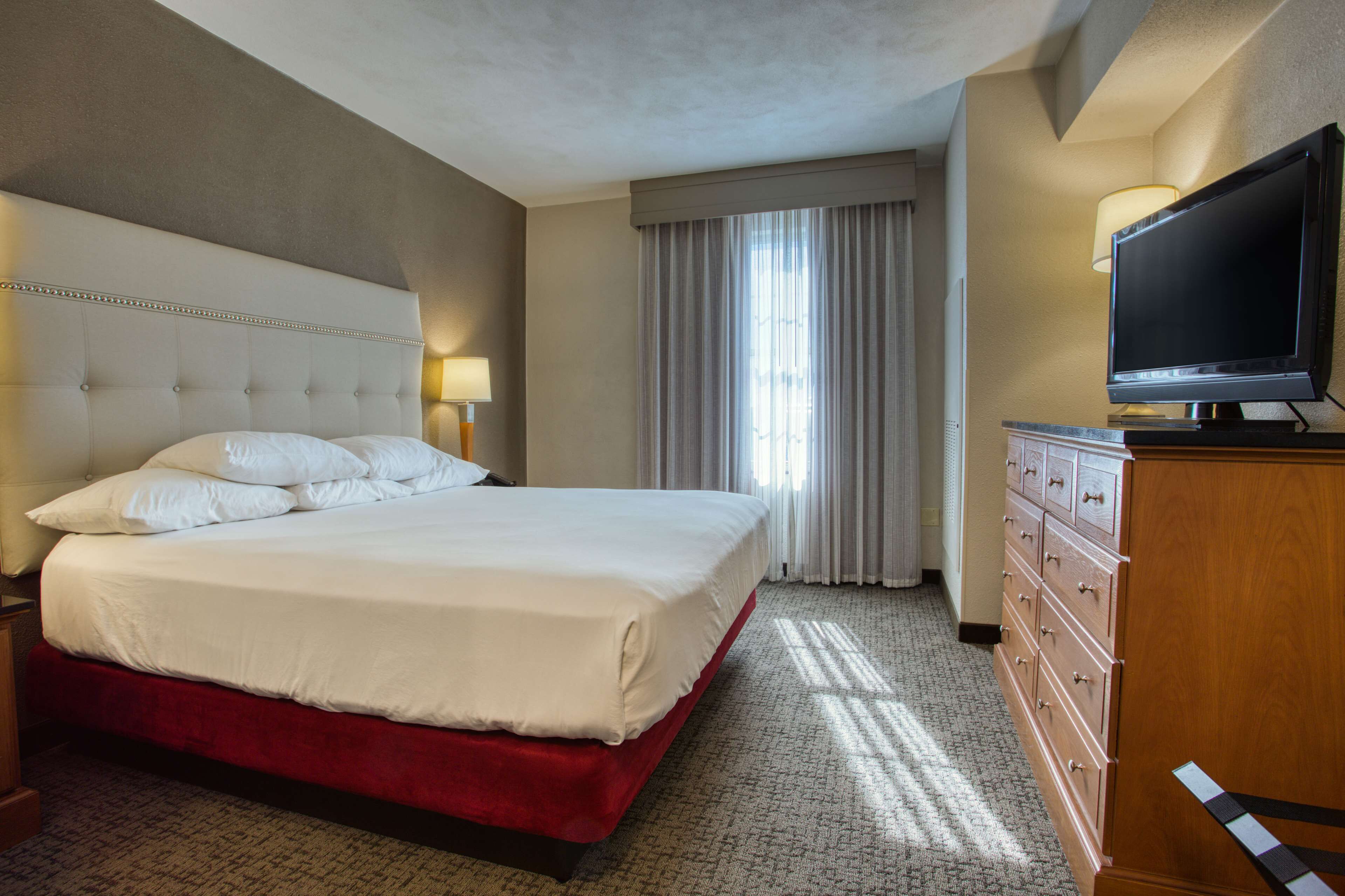 Habitación de hotel con una cama grande, televisor, cómoda y ventana con cortinas.