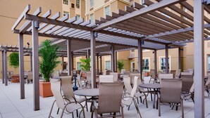 Een terras buiten met meerdere tafels en stoelen, overdekt door een pergola.