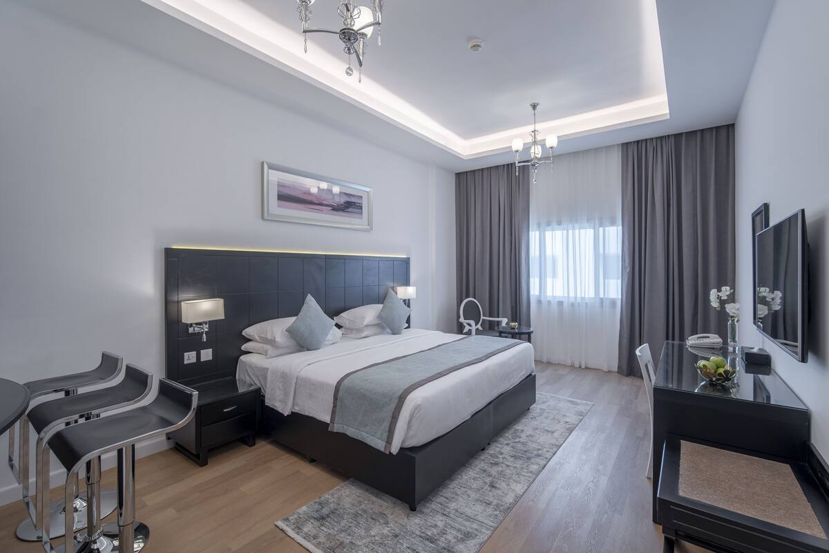 A modern bedroom with a large bed, bedside tables, a desk, and a chandelier.