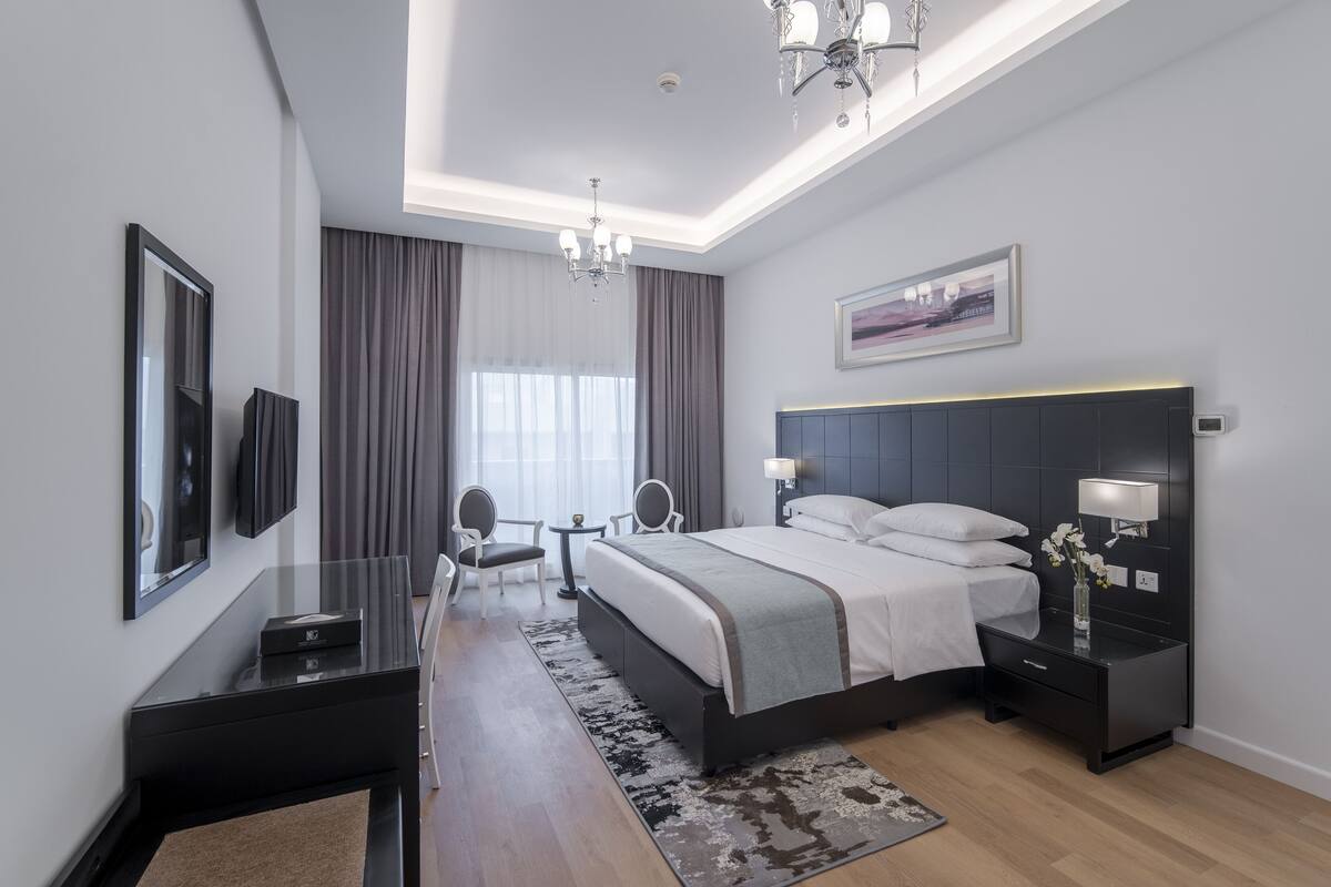 A modern hotel room with a large bed, bedside tables, a desk, and a chandelier.