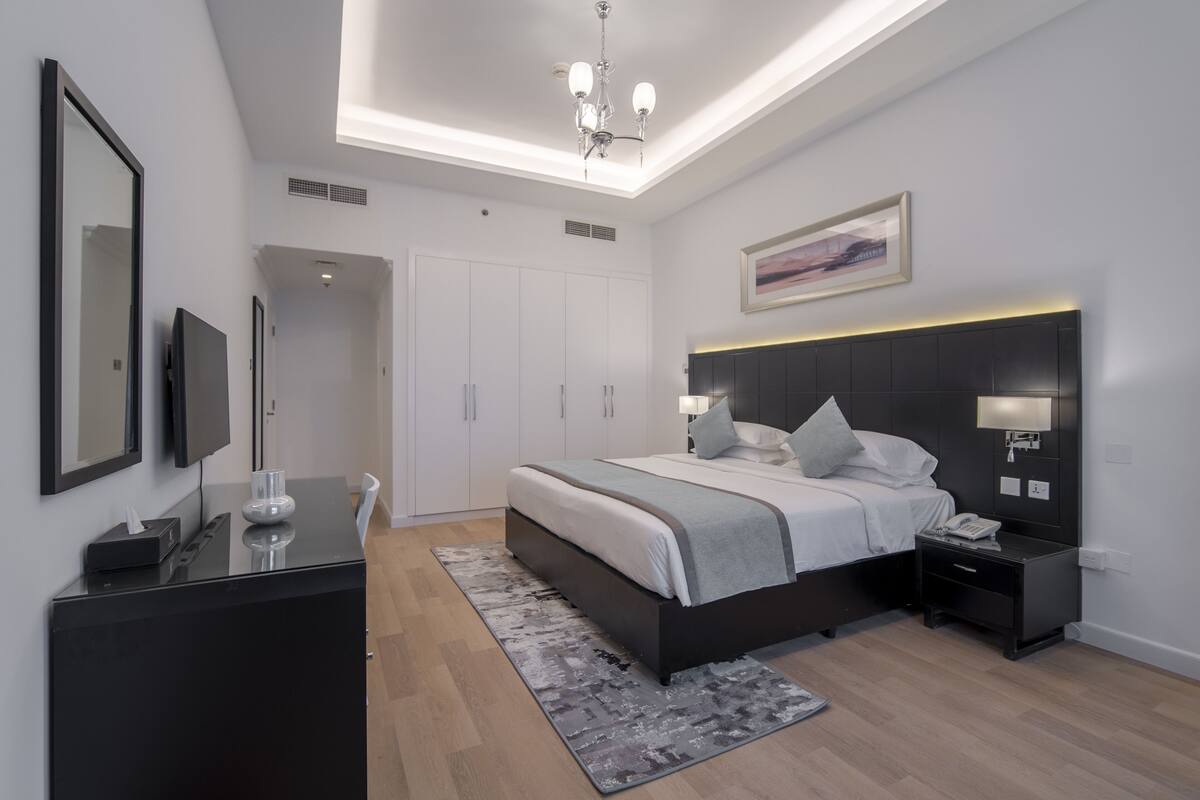 A modern bedroom with a bed, bedside tables, a desk, and a TV.