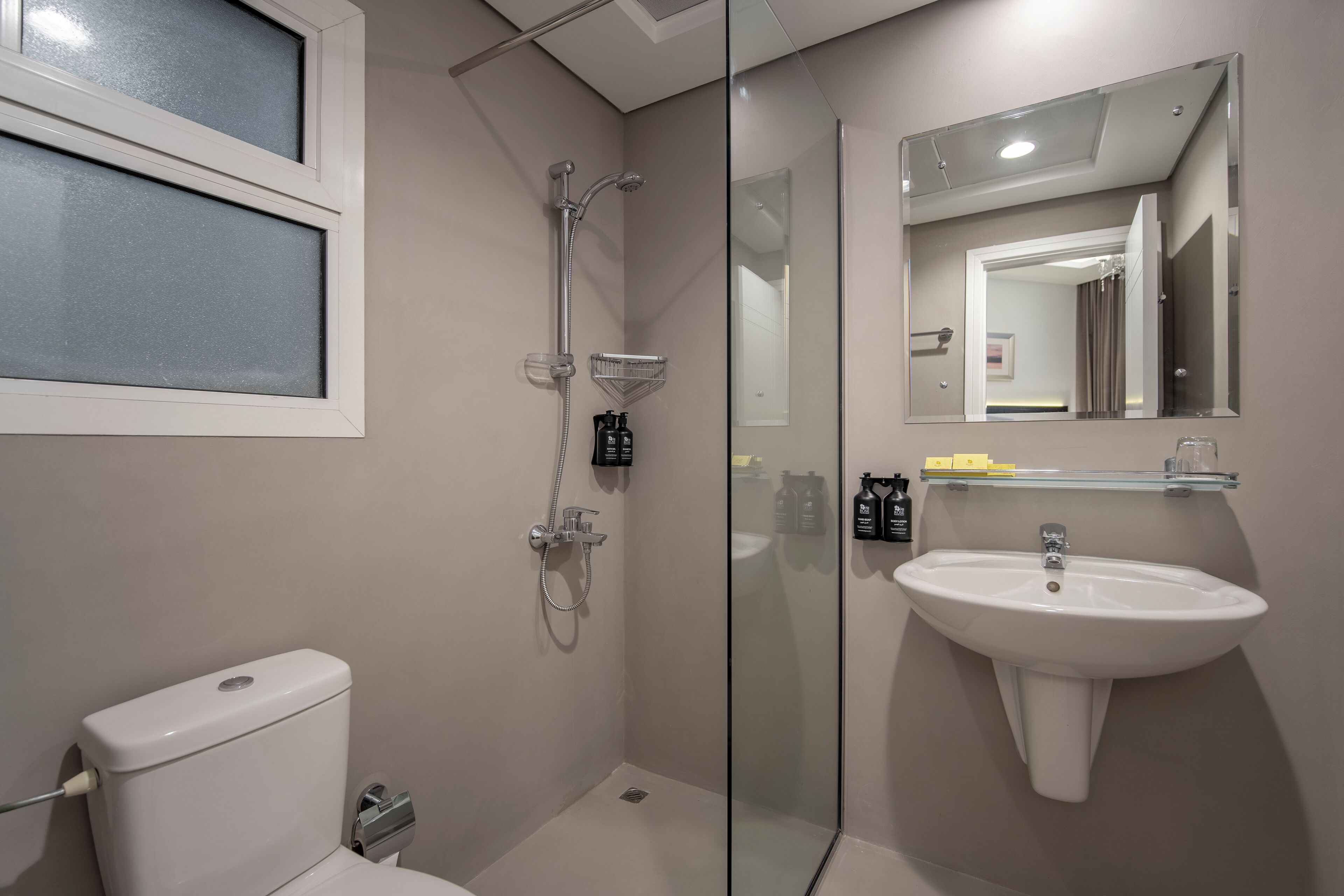 Une salle de bain moderne avec une douche à parois de verre, des toilettes et un lavabo surmonté d’un miroir.