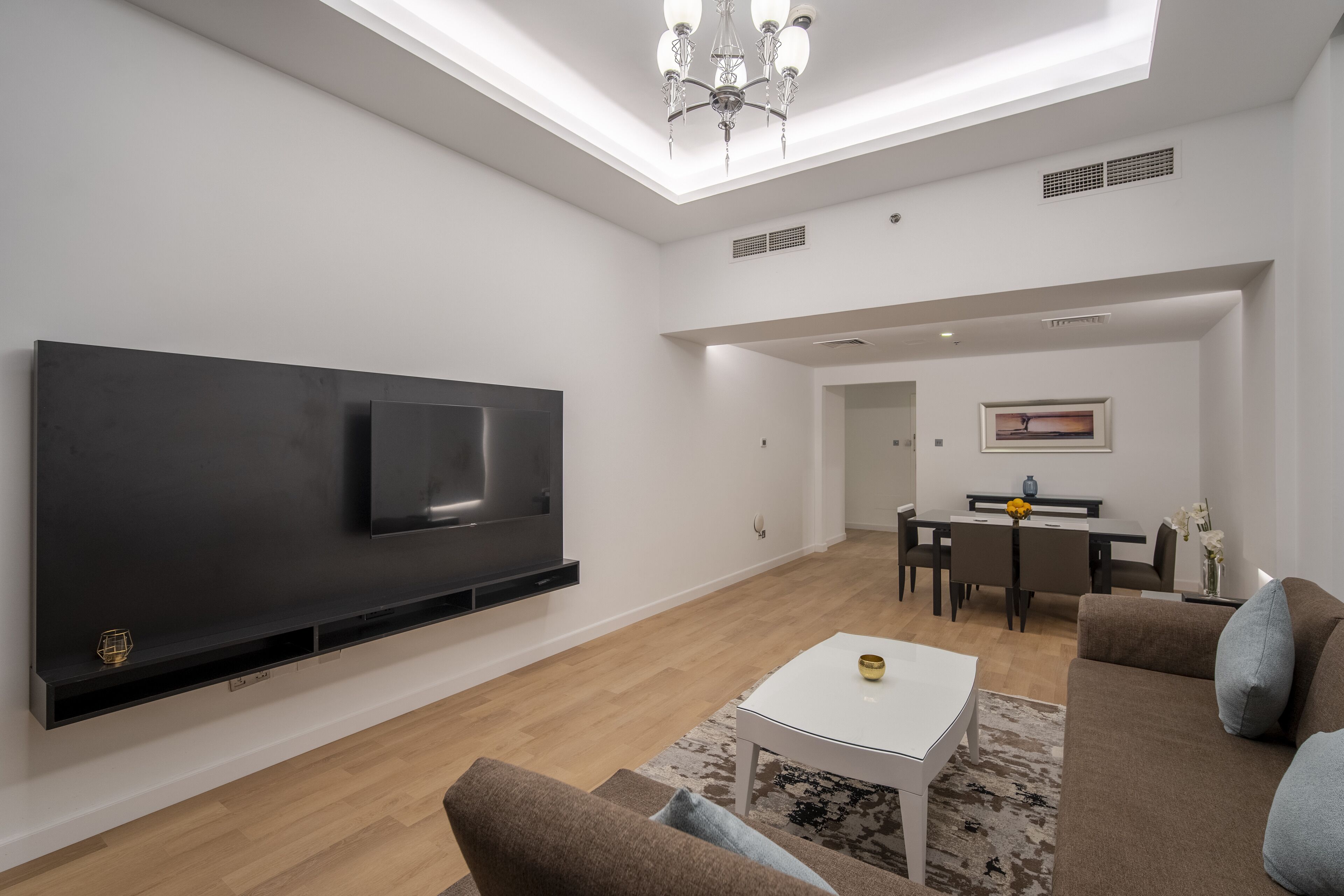 Uma sala de estar moderna com televisão de tela plana, uma mesa de centro branca e um sofá marrom.