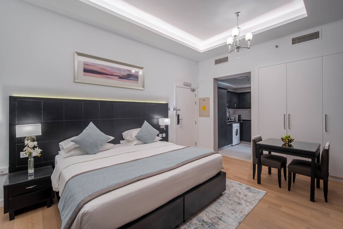 A modern bedroom with a large bed, bedside tables, a desk, and a dining area.