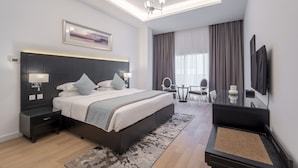 A modern hotel room with a large bed, bedside tables, a desk, a chair, a TV, and a large window with curtains.