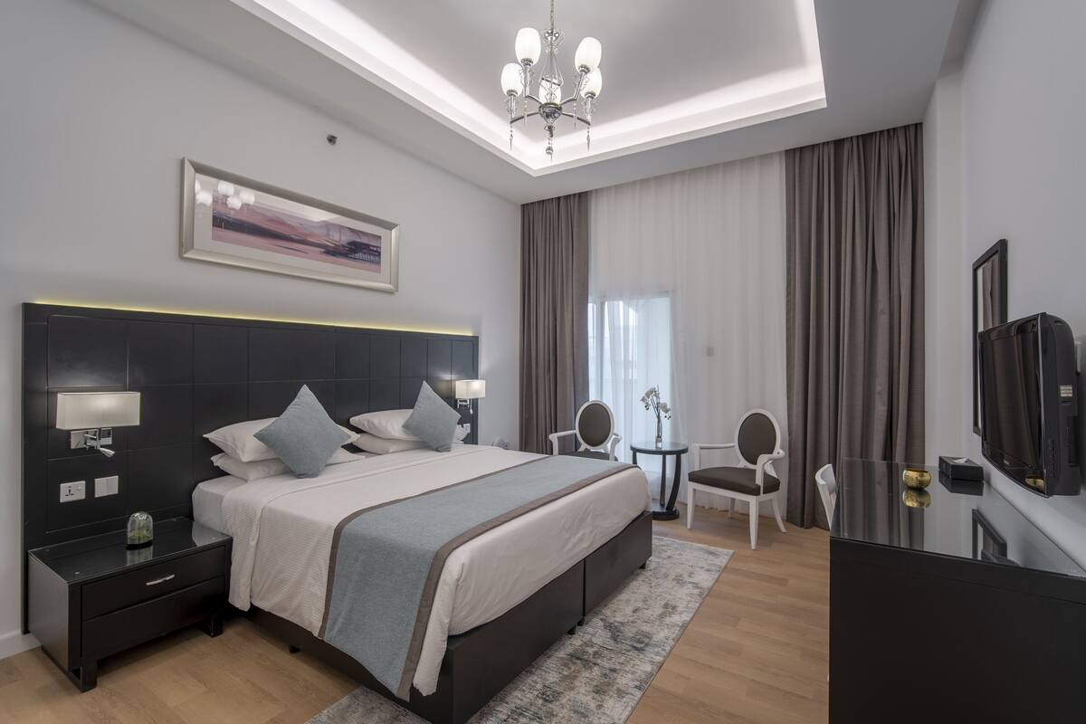 A modern hotel room with a large bed, bedside tables, a desk, and a TV.