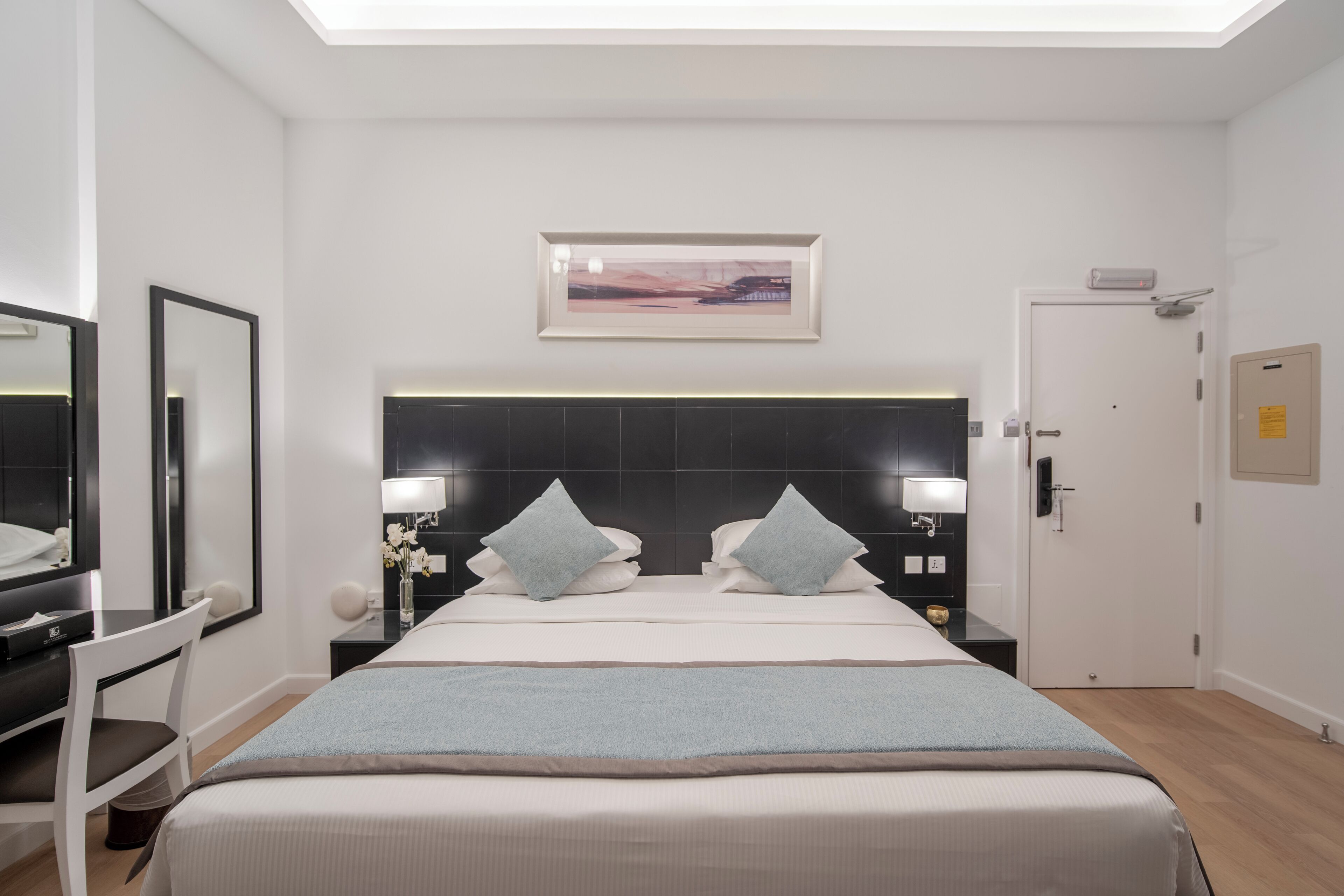 A modern hotel room with a large bed, a desk, a chair, and a mirror.