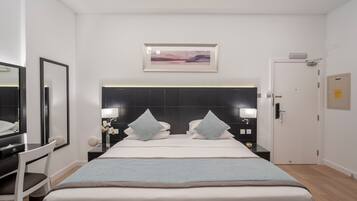 A modern hotel room with a large bed, a desk, a chair, and a mirror.