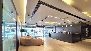 A modern reception area with a curved seating area, a reception desk with two staff members, and a large glass window offering a view of the street.