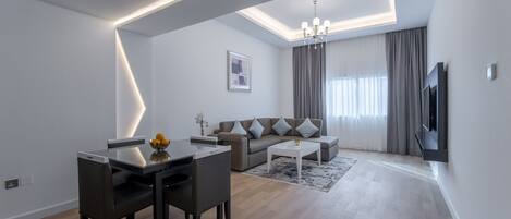 A modern living room with a dining area, a sofa set, a flat-screen TV, and a chandelier.