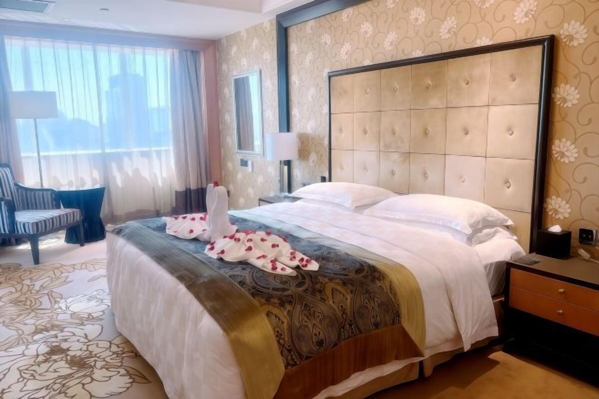 Een hotelkamer met een groot bed, een nachtkastje, een stoel en een raam met gordijnen.